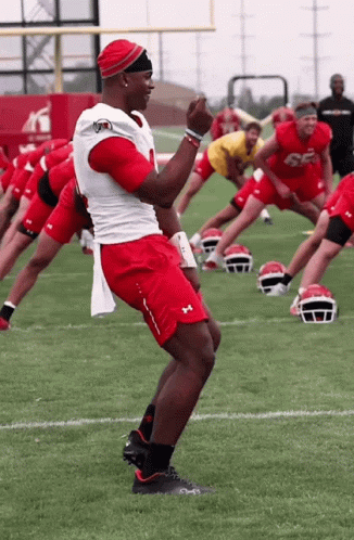 A Group Of Football Players Are Stretching On The Field And One Of Them Has The Number 56 On His Jersey GIF