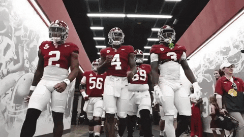 A Group Of Football Players Are Walking Down A Hallway GIF