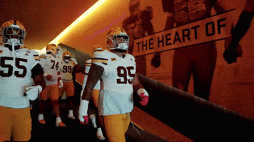 a group of football players are walking down a hallway with a sign that says the heart of