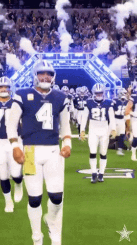 A Group Of Football Players Are Walking On A Field With Smoke Coming Out Of The Tunnel . GIF