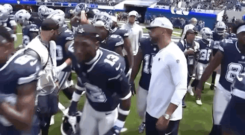 A Group Of Football Players Are Walking On A Field With Their Coach . GIF
