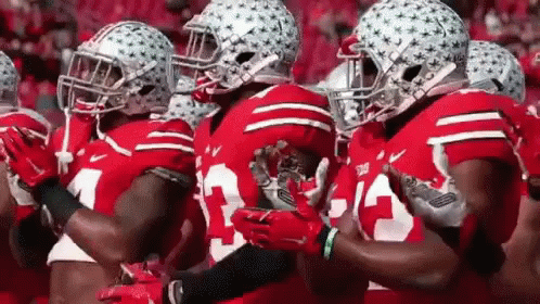 a group of football players wearing red jerseys and helmets are standing in a line .