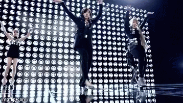 A Group Of Girls Are Dancing In Front Of A Wall Of Lights . GIF
