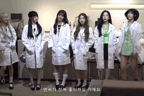 A Group Of Girls In Lab Coats Are Standing In A Line GIF