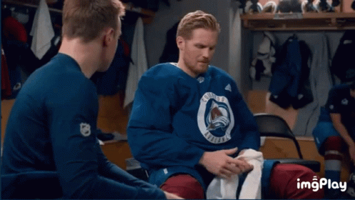 a group of hockey players are sitting in a locker room with the colorado avalanche logo on a wall