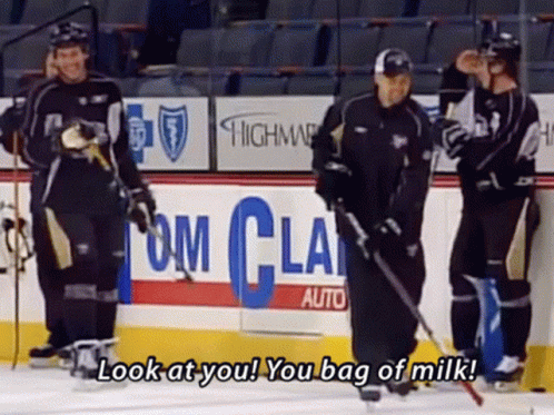 A Group Of Hockey Players Are Standing On A Rink With A Sign That Says Look At You You Bag Of Milk GIF