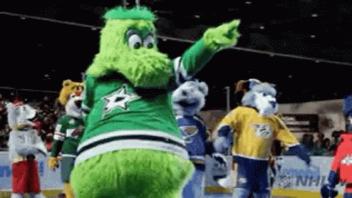 A Group Of Mascots Are Standing On A Ice Rink And One Of Them Is Pointing . GIF