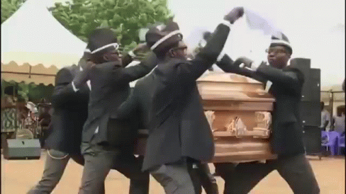 A Group Of Men Are Dancing Around A Coffin In A Cemetery . GIF
