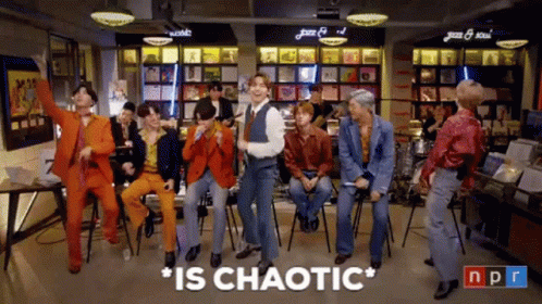A Group Of Men Are Dancing In A Room With The Words " Is Chaotic " Above Them GIF