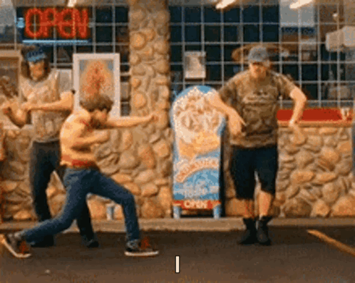 a group of men are dancing in front of a store with an open sign .