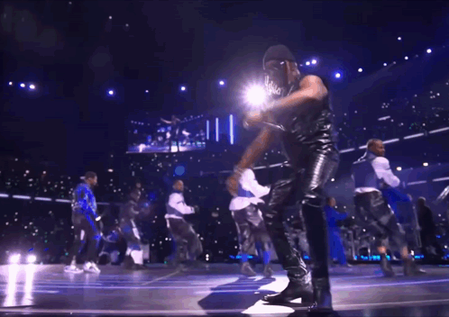 A Group Of Men Are Dancing On A Stage In Front Of A Large Screen GIF