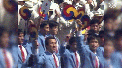 A Group Of Men Are Holding Up Their Fans In Front Of The Olympics Logo GIF