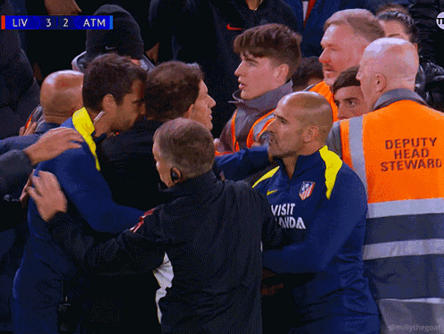 A Group Of Men Are Huddled Together With One Wearing An Atm Shirt GIF