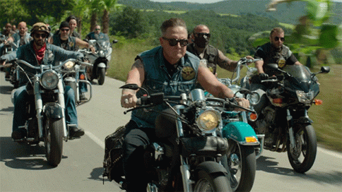 a group of men are riding motorcycles down a road with one man wearing sunglasses