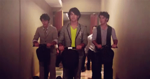 A Group Of Men Are Riding Scooters In A Hallway GIF