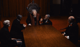 A Group Of Men Are Sitting Around A Table With A Man Standing In The Middle GIF