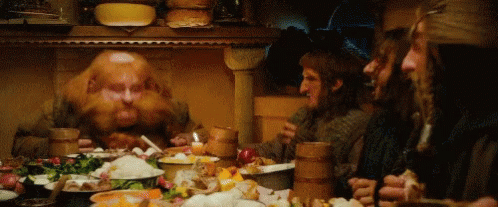 A Group Of Men Are Sitting Around A Table With Plates Of Food . GIF