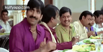 a group of men are sitting at a long table eating food .