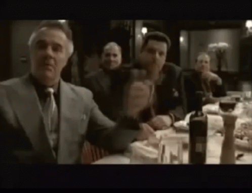 A Group Of Men Are Sitting At A Table Drinking Wine And Eating Food . GIF