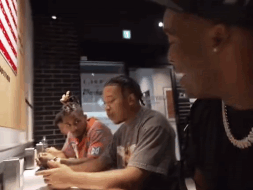 A Group Of Men Are Sitting At A Table With One Wearing A T-Shirt That Says Do GIF
