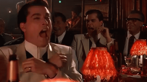 A Group Of Men Are Sitting At A Table With Red Lamps And Laughing GIF