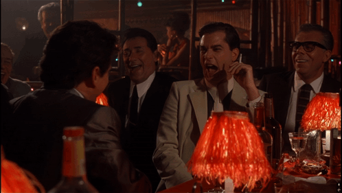 A Group Of Men Are Sitting At A Table With Red Lamps In A Dark Room GIF