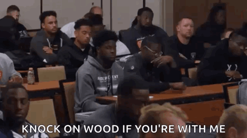 A Group Of Men Are Sitting At Tables In A Classroom With The Words `` Knock On Wood If You 'Re With Me '' GIF