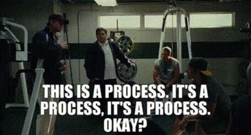 A Group Of Men Are Sitting In A Gym Talking About A Process GIF