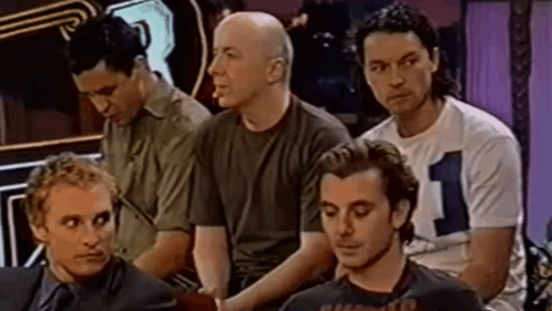A Group Of Men Are Sitting In A Row And One Of Them Is Wearing A Shirt With The Number 1 On It . GIF