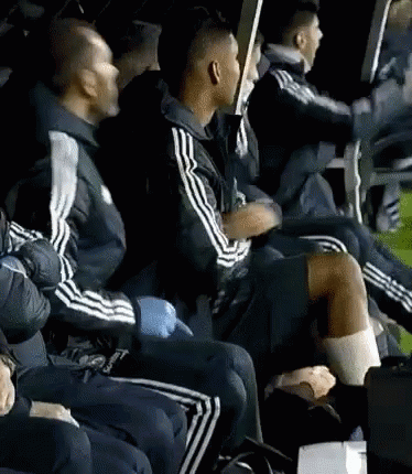 a group of men are sitting in a row wearing adidas jackets