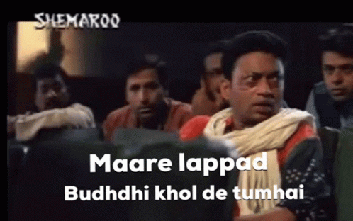 A Group Of Men Are Sitting In A Theater Watching A Movie And One Of Them Is Wearing A White Scarf Around His Neck . GIF