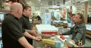 A Group Of Men Are Standing Around A Counter In A Store That Says History On The Bottom GIF