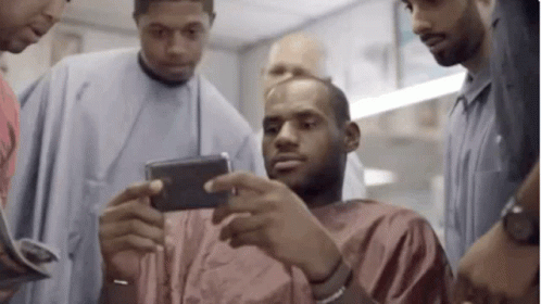 A Group Of Men Are Standing Around A Man In A Barber Shop . GIF