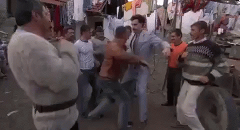 A Group Of Men Are Standing Around A Man In A Suit Dancing On A Street . GIF