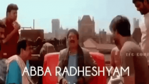 A Group Of Men Are Standing Around A Red Couch And Talking To Each Other . GIF