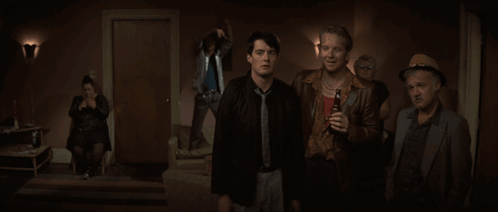 A Group Of Men Are Standing In A Dark Room And One Of Them Is Holding A Bottle Of Beer GIF