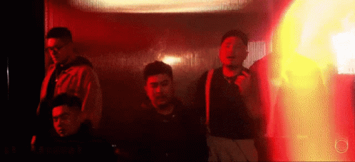 A Group Of Men Are Standing In A Dark Room With A Red Light Behind Them . GIF