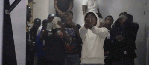 A Group Of Men Are Standing In A Room And One Of Them Is Wearing A Hoodie With The Number 18 On It . GIF