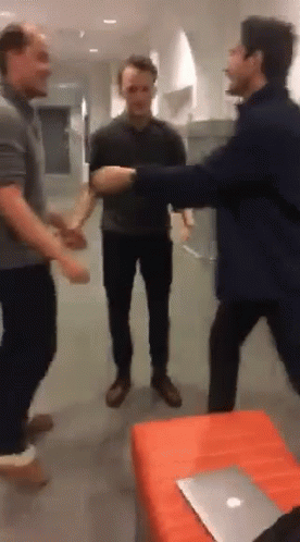 A Group Of Men Are Standing In A Room With A Laptop On The Table GIF
