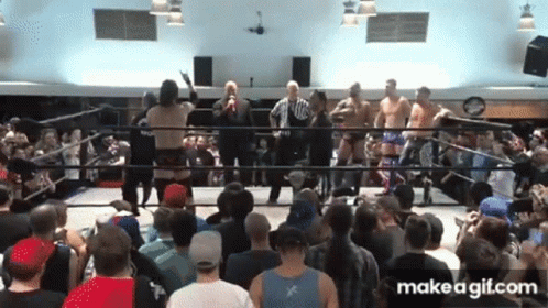 A Group Of Men Are Standing In A Wrestling Ring With A Crowd Watching GIF