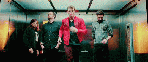 A Group Of Men Are Standing In An Elevator . One Of The Men Is Wearing A Red Jacket . GIF
