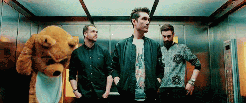 A Group Of Men Are Standing In An Elevator With A Teddy Bear In The Background . GIF