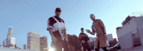 A Group Of Men Are Standing In Front Of A City Skyline And One Of Them Is Wearing A Shirt That Says Supreme On It GIF