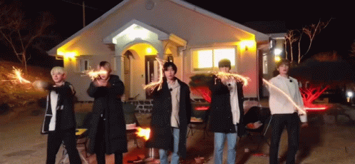 a group of men are standing in front of a house holding sparklers .