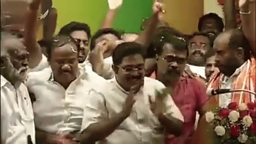 A Group Of Men Are Standing In Front Of A Microphone With Their Arms In The Air GIF