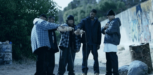 A Group Of Men Are Standing In Front Of A Trash Can That Says Warning On It GIF