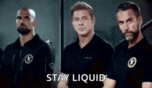 A Group Of Men Are Standing Next To Each Other In A Room With The Words `` Stay Liquid '' Written On The Screen . GIF