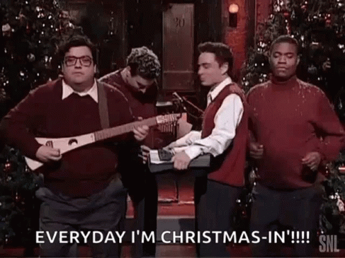 A Group Of Men Are Standing Next To Each Other In Front Of A Christmas Tree . One Man Is Playing A Guitar . GIF