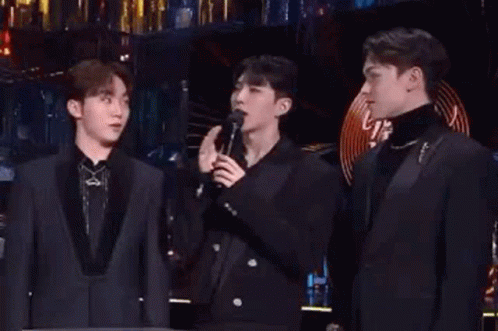 A Group Of Men Are Standing Next To Each Other On A Stage Singing Into Microphones . GIF