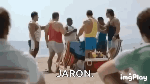 A Group Of Men Are Standing On A Beach Talking To Each Other And Jaron Is Standing In The Middle Of The Group . GIF